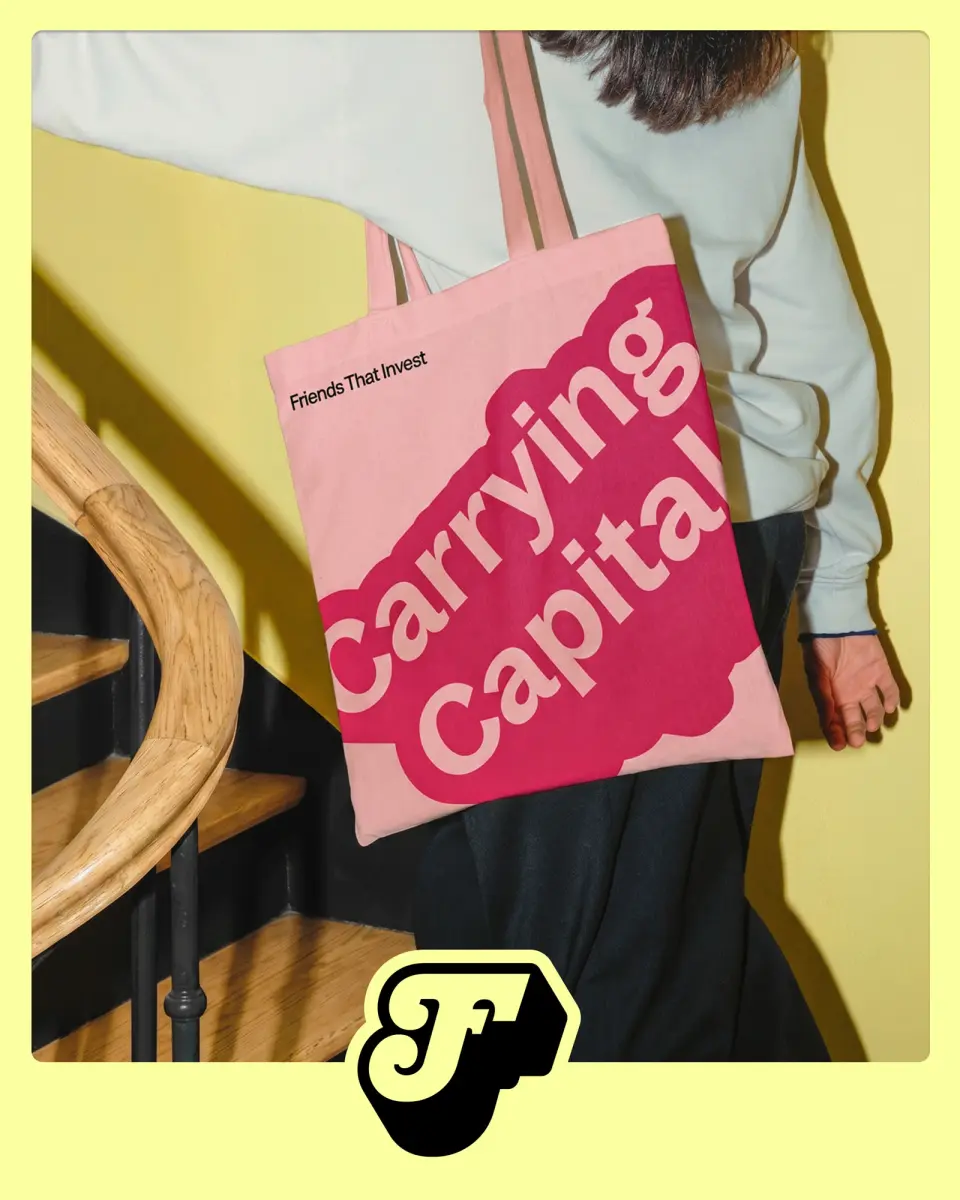 Pink tote bag printed “Carrying Capital” held against a yellow background