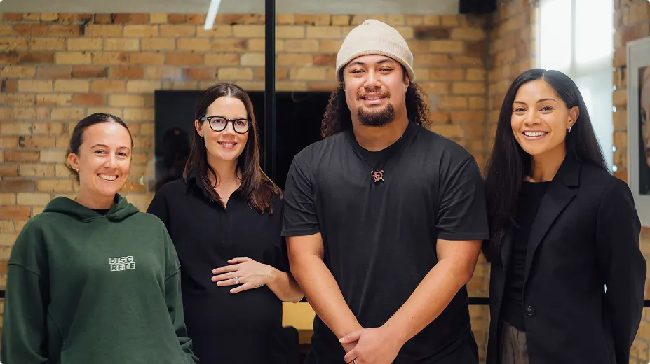 Four smiling people standing together in a brick-walled office