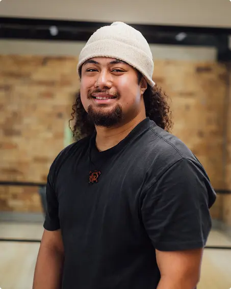 Smiling man in a beanie and black t-shirt in a brick-walled office