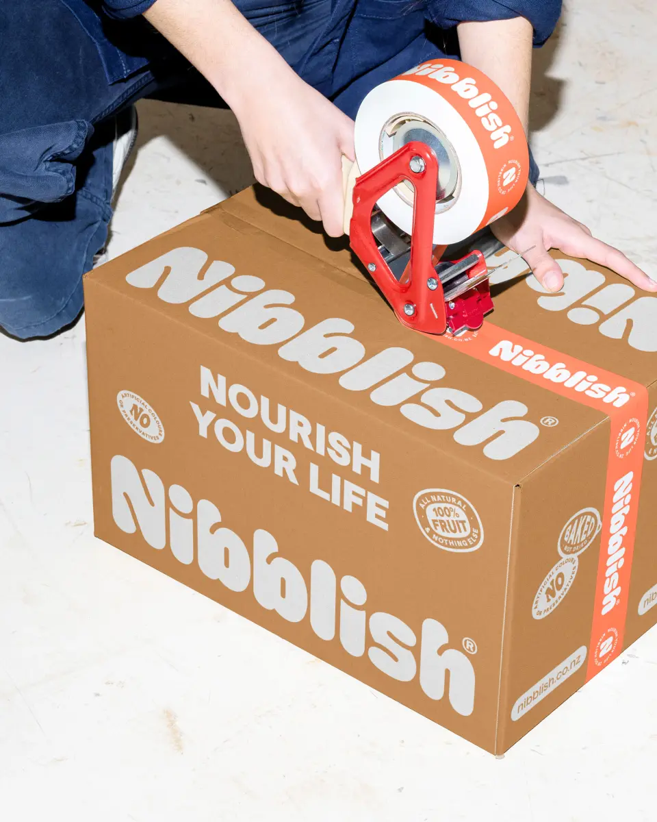 Hands taping a Nibblish shipping box that reads “Nourish your life”