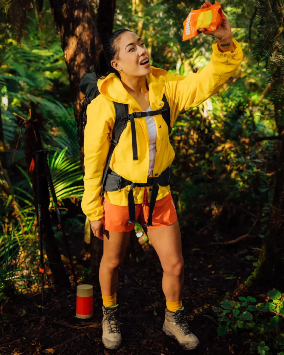 Person in a yellow jacket and harness reaching into trees