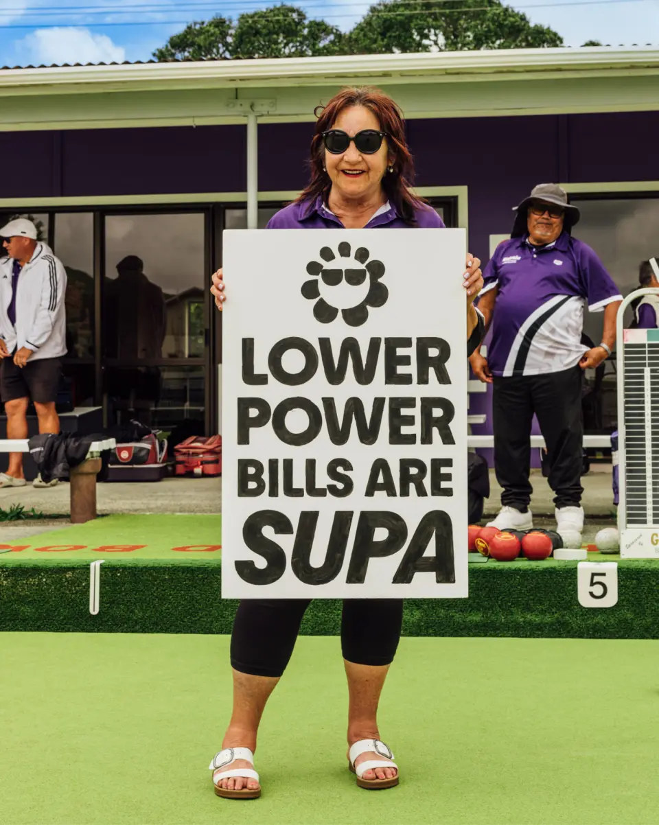 Woman holding a “Lower power bills are Supa” sign on a bowling green